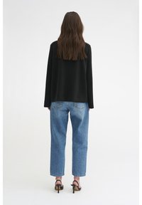 Černá oversized mikina, volný střih, v kombinaci se světle modrými džíny s vysokým pasem. Hladký materiál, tříčtvrteční rukávy, minimalistický design.