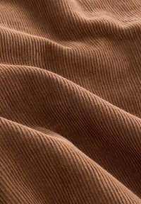 Bruine corduroy stof met een duidelijke verticale ribbeltextuur, voorzien van zachte plooien en een gladde afwerking, geschikt voor verschillende textieltoepassingen.