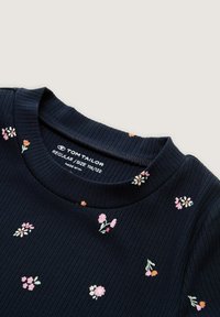 Navy geribbelde trui met bloemstickers in roze, oranje en wit; ronde halslijn met een label waarop merk- en maatgegevens staan.