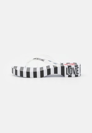 Tongs en plastique transparent avec une plateforme à rayures noires et blanches, arborant la marque "LOVE MOSCHINO" sur le côté et à l'avant.