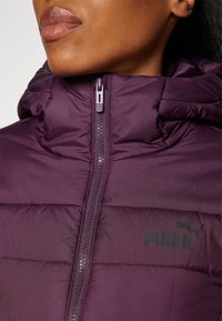 Giacca puffer prugna con colletto alto, chiusura a zip e logo a sbalzo. Il tessuto presenta una consistenza liscia e orli cuciti in tutta la giacca.