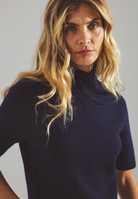 Tumed sinise lühikeste varrukatega turtleneck-sviiter ribakaartega tekstuuriga ja kehakujulise disainiga, valmistatud villast või sarnastest pehmetest materjalidest. Korralik viimistlus.