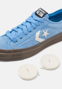 Sneaker bassa in suede blu con logo a stella bianca, lacci tondi e suola marrone scuro. Include due paia extra di lacci bianchi.
