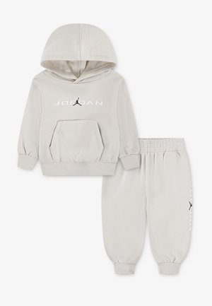 Svetlo sivi dukserica i trenerke. Dukserica ima prednji dzep, rebraste manžete i "JORDAN" logo sa crnim Jumpman grafikom.