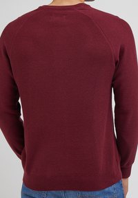 Pull bordeaux avec un design en maille texturée, manches longues, bords-côtes aux poignets et à l'ourlet. Tissu lisse avec une construction de manches raglan.