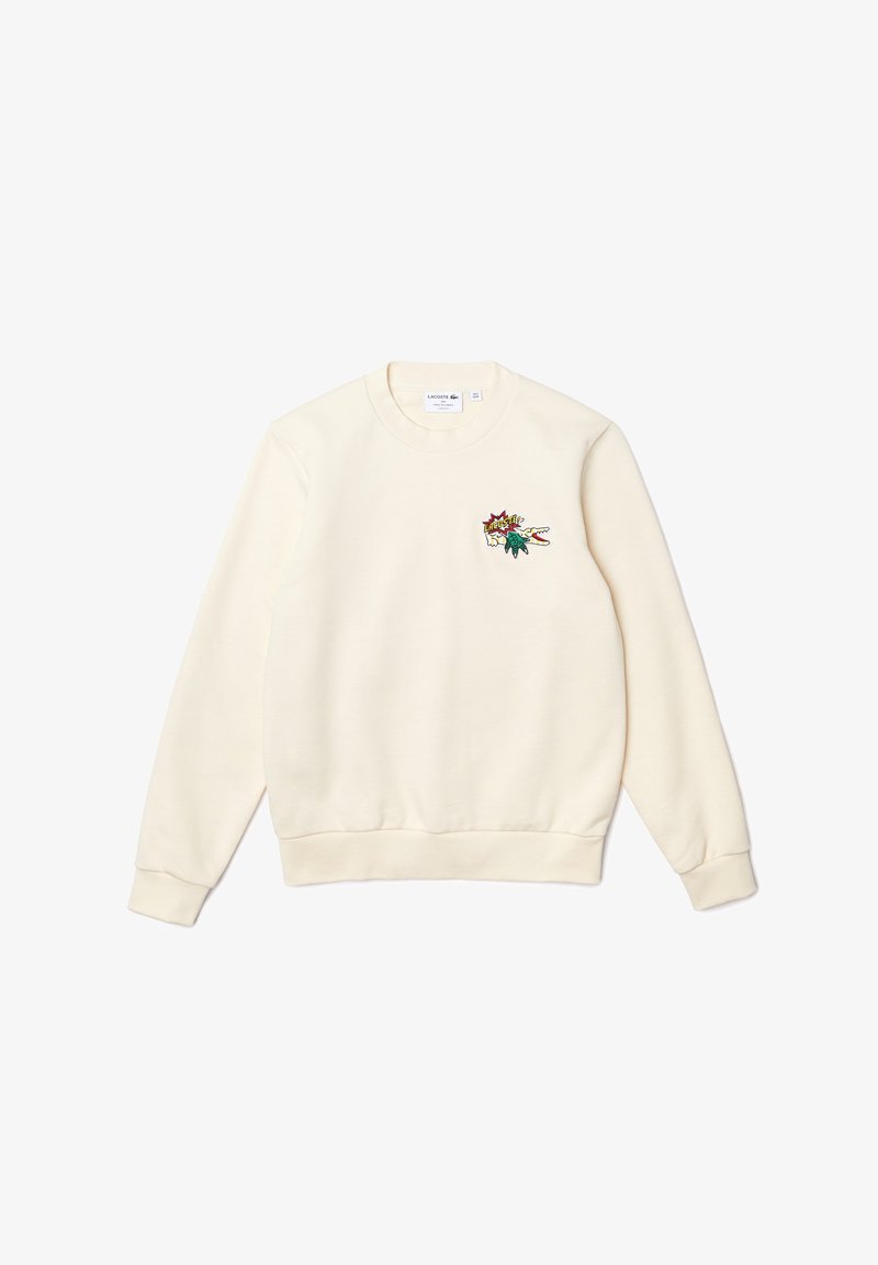 Sweat-shirt blanc cassé à manches longues et col rond, avec petit logo Lacoste coloré représentant un crocodile en dessin animé sur le côté gauche de la poitrine.