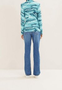 Maglietta a maniche lunghe color turchese, con motivi astratti a onde. Abbinata a jeans a zampa d'elefante blu e sneakers bianche. Design semplice, vestibilità casual.