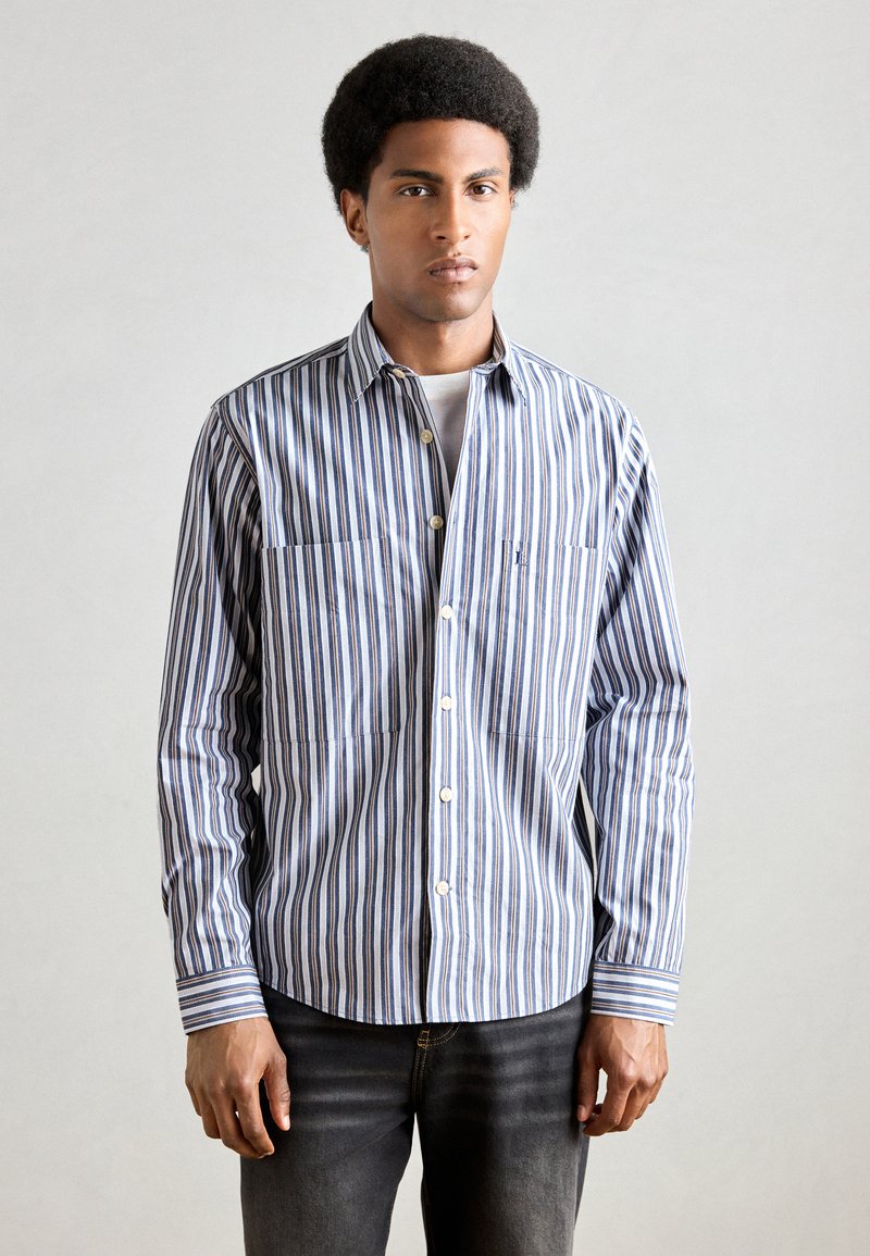 Kék és fehér csíkos ing, gombos kialakítással, két mellzsebbel és hosszú, csukló részletű ujjakkal.