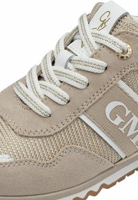 Beige sneaker met een bovenwerk van textuurstof, witte vetersluiting, metallic gouden accenten en een wit logo aan de zijkant. Rubberen loopzool met profiel.