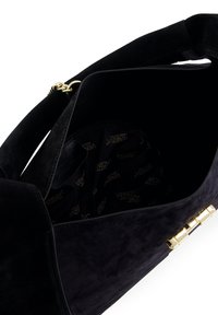 Sac à main en daim noir avec ferrures dorées, intérieur spacieux avec doublure en tissu de marque et design structuré. Détail de la fermeture visible.