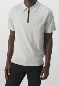Svetle šedé polo tričko s krátkým rukávem, límcem a zipovým zapínáním. Obsahuje pruhovaný akcent na zipu a žebrovaný lem.