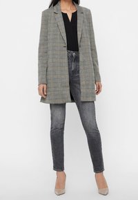 Kostkovaný blejzr v šedé a béžové látce, s uvolněným střihem, klopovými límci a zapínáním na jeden knoflík, spárovaný s tmavými džíny.