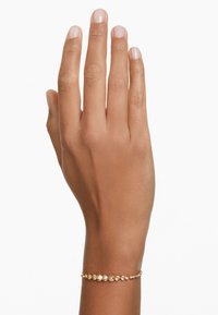 Złota bransoletka z wieloma małymi okrągłymi kamieniami szlachetnymi, z delikatnym krojem łańcucha i polerowanym wykończeniem, noszona na nagiej dłoni.