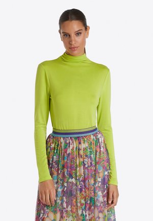Langärmliges Rollkragenoberteil in lebhaftem Limettengrün, kombiniert mit einem mehrfarbigen Blumenkleid mit einem strukturierten Taillenbund.