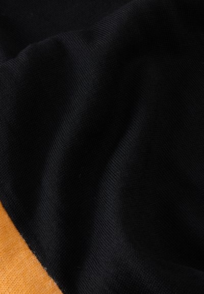 Κοντινή λήψη μαύρου πλεκτού υφάσματος με μια μικρή ορατή άκρη πορτοκαλί πλεκτού υφάσματος σε μια γωνία.