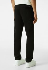 Svarta cargobyxor med rak passform, som har två sidfickor, bakfickor och en slät yta. Bärs med vita sneakers.