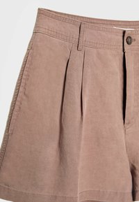 Shorts plissettati in un morbido tessuto rosa tenue. Presentano una vita standard con chiusura a bottone e una texture liscia.