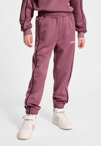 Lilla sweatpants med en afslappet pasform, elastisk talje og manchetter ved anklerne. Har sorte sidelister og et lille hvidt logo på benet.