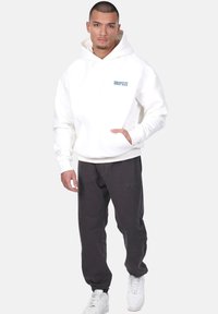 White hoodie with "DROPSIZE" logo, front pocket, paired with dark gray sweatpants featuring embossed brand name and elastic cuffs.