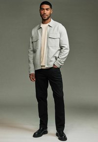 Light grey zip-up jacket with two chest pockets, layered over a cream knit sweater, paired with black pants and black chunky boots.