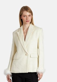 Blazer de lana crema con silueta estructurada, solapas con muesca, dos bolsillos frontales, botón de perla y acentos de piel sintética en las mangas.
