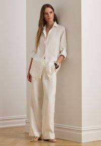 Balti lininių marškinių su mygtukais, suvyniotomis rankovėmis, derinami su laisvo kirpimo lino kelnėmis. Paprastas dizainas; dėvima su minkštomis basutėmis ir aksesuarais.