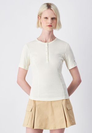 Haut blanc à rayures, à manches courtes, avec un col rond et une patte de boutonnage, associé à une jupe plissée beige dotée de poches latérales.