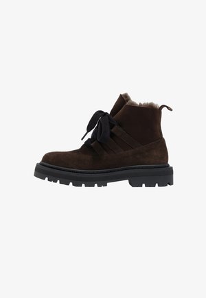 Botines de ante marrón con cordones negros, forro peludo y una suela gruesa de goma negra con tacos profundos para mejorar la tracción.