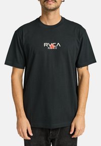Černé bavlněné tričko má na hrudi malé logo RVCA v bílé a červené barvě. Krátké rukávy, kulatý výstřih a volný střih.
