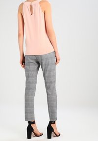 Top rosa claro sin mangas con detalle de abertura en la espalda, combinado con pantalones de vestir gris a cuadros y sandalias negras de tacón.