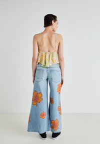 Top de tanque leve com estampado floral e alças finas, combinado com jeans de corte amplo, azul claro, com padrões de hibiscos laranja.