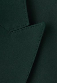 Ciemnozielona tkanina prezentuje gładką fakturę z widocznym przeszyciem wzdłuż krawędzi, z ostrym, spiczastym narożnikiem.