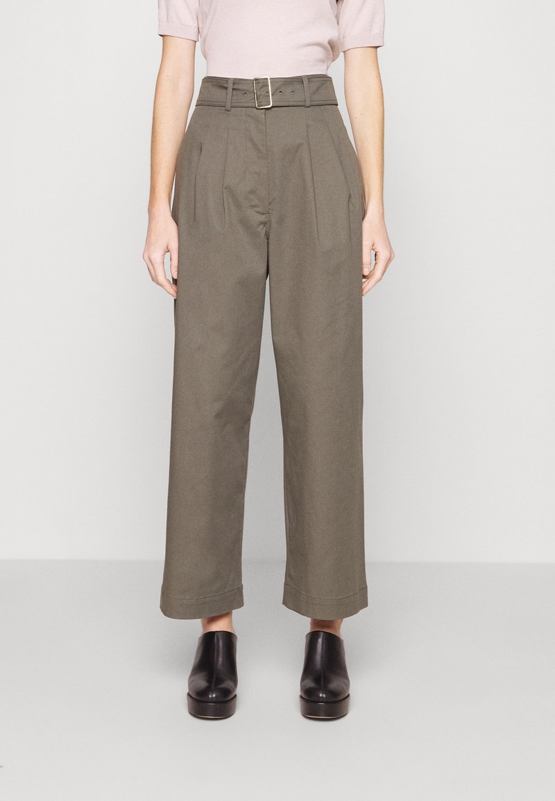 Pantalons taille haute à jambes larges en coton vert olive avec des plis, une taille ceinturée et une coupe droite se terminant juste au-dessus de la cheville, associés à des chaussures noires.