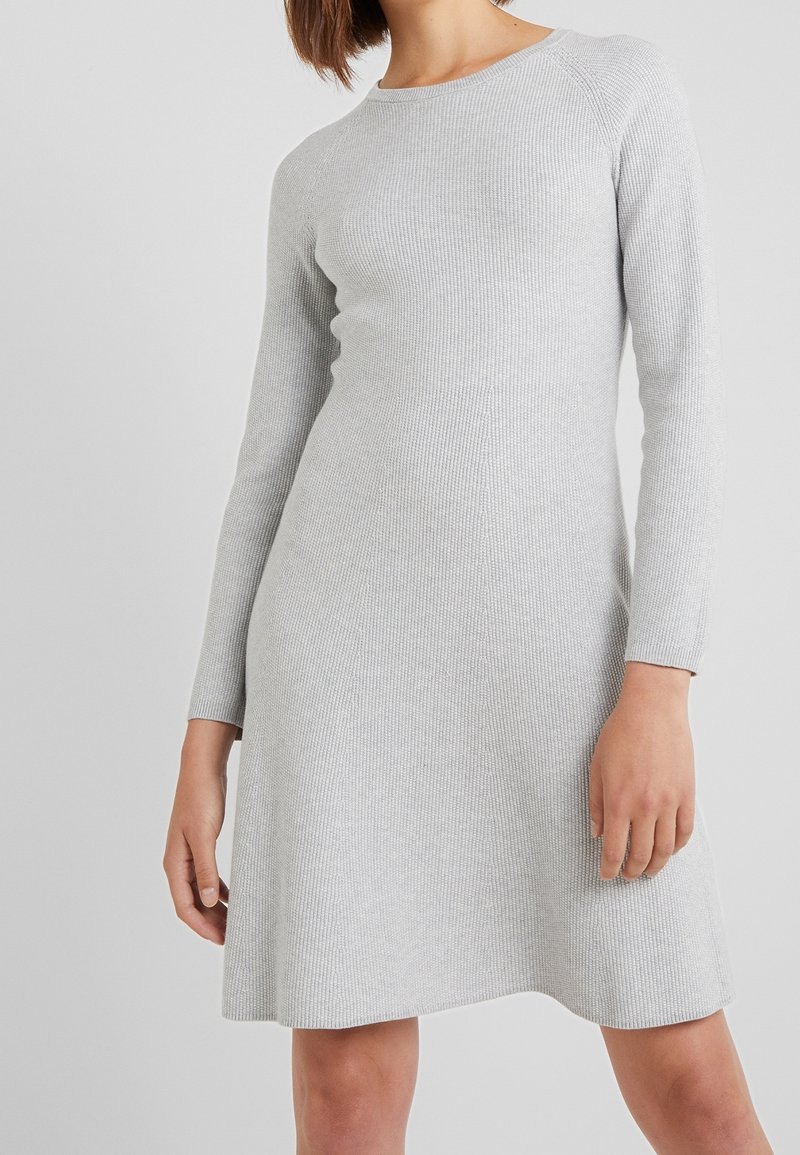 Ljusgrå, långärmad ribbad stickad klänning med rak silhuett, rund halsringning och subtil struktur, som flädrar något vid fållen.