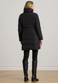 Svart puffjacka med hög krage, midjebälte och quiltad textur. Kombinerad med svarta höga stövlar och tajta byxor.