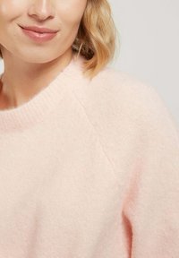 Pull en laine rose clair, doux, avec un col rond et des finitions côtelées. Présente une coupe décontractée et une surface légèrement texturée.