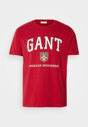 Czerwona bawełniana koszulka z odważnym białym logo "GANT", tarczą z napisem "USA 1949" oraz tekstem "AMERICAN SPORTSWEAR" poniżej. Klasyczny dekolt typu crew neck.