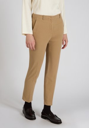 Lichtbruine op maat gemaakte broeken met een gladde textuur, voorzakken en een getailleerde pasvorm. Gepaard met donkere instapschoenen en zichtbare enkelsokken.