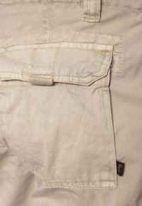 I pantaloni cargo in cotone beige presentano una tasca posteriore con pattina, cuciture rinforzate e un'etichetta laterale. Tessuto morbido con un design casual.