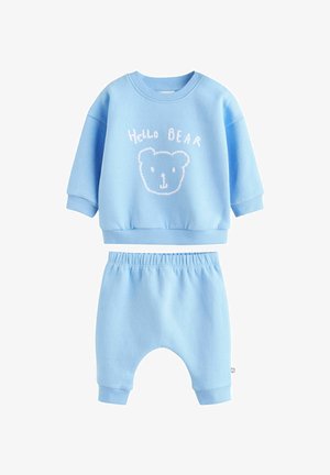 Conjunto de dos piezas en azul claro que presenta un sudadera de manga corta con un gráfico de oso y pantalones estilo jogger a juego con una cintura elástica.