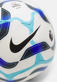 Nogometna žoga Nike z belo površino, črnimi logotipom Swoosh in modrimi abstraktnimi vzorci. Ima teksturirane heksagonalne panele in logo Premier League.