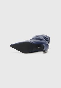 Cizmă din piele de culoare bleumarin, până la genunchi, cu vârf ascuțit, având un toc mic și textură strânsă pe ax. Talpă solidă din cauciuc negru.