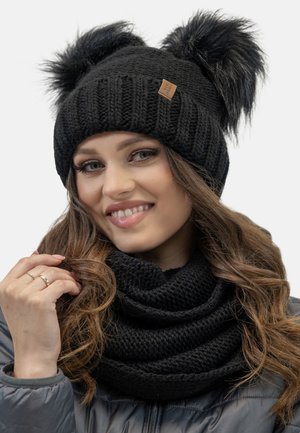 Czarna dziana czapka z dwoma futrzanymi pomponami i teksturowanym wzorem, w połączeniu z czarnym dzianinowym szalikiem w stylu infinity, prezentująca przytulny zimowy wygląd.