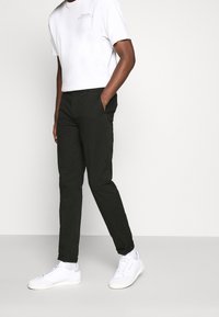 Pantalons noirs slim avec une texture lisse, associés à un t-shirt blanc à col rond et à des baskets blanches. Comprend des poches latérales et un design épuré.