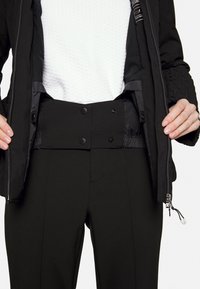 Black zip-up jacket with quilted texture. Interior features a smooth black lining. Black high-waisted pants with snap closures and straight legs.