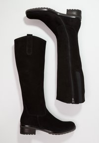 Bottes en suede noires montantes jusqu'aux genoux avec talons bloc, fermeture éclair latérale et tirette, présentées sur un fond blanc.