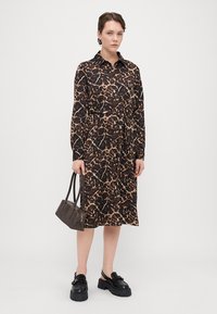 Rochie cu mâneci lungi, de culoare maronie, cu un model leopard, talie strânsă, guler cu nasturi, asortată cu o geantă mică gri și pantofi negri cu talpă groasă.