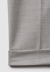 Gros plan sur une jambe de pantalon en tissu gris clair avec un revers soigneusement plié, montrant un tissage finement texturé et une couture propre.