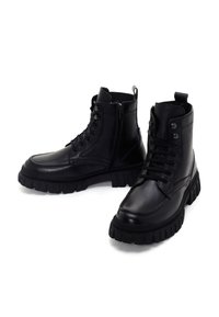 Botas de tobillo de cuero negro con una suela de goma resistente, con cierre de cordones y cremallera, acabado texturizado y detalles de diseño robusto.