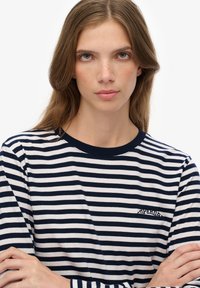 Langærmet T-shirt i marineblå og hvid stribe lavet af bomuld. Har en marineblå rund hals og et lille logo på brystet. Blød tekstur.